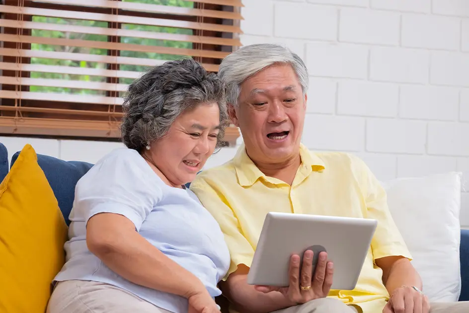 An older couple sitting on a sofa looking at something on a digital tablet.