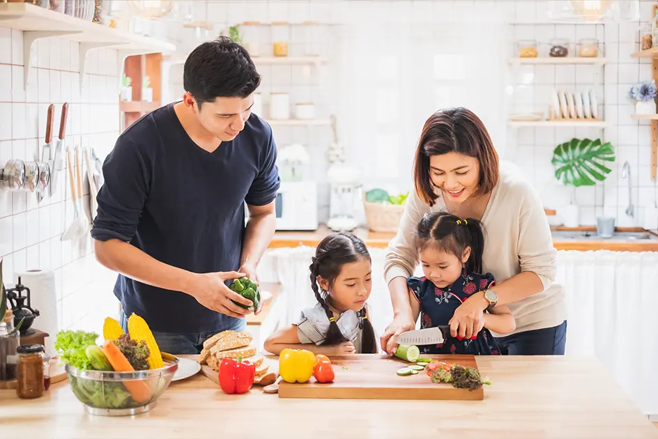 A father and a mother with their two children in the kitchen cutting up vegetables.