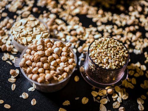 Three containers holding different types of grains with oatmeal scattered around the table.