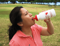 A woman drinking from a bottle at the park.