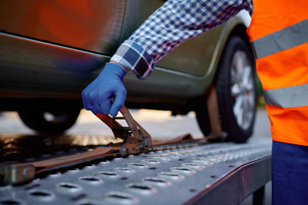 Closeup tow truck driver hand fixing car with belt on platform. Roadside assistance concept