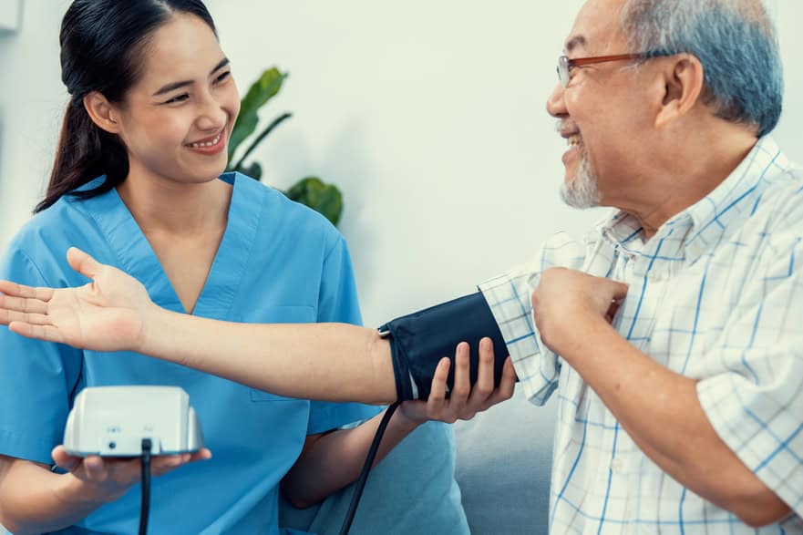 A contented retired man having a blood pressure check by his personal caregiver at his home with a smiley face. Senior care at home, nursing home for pensioners.