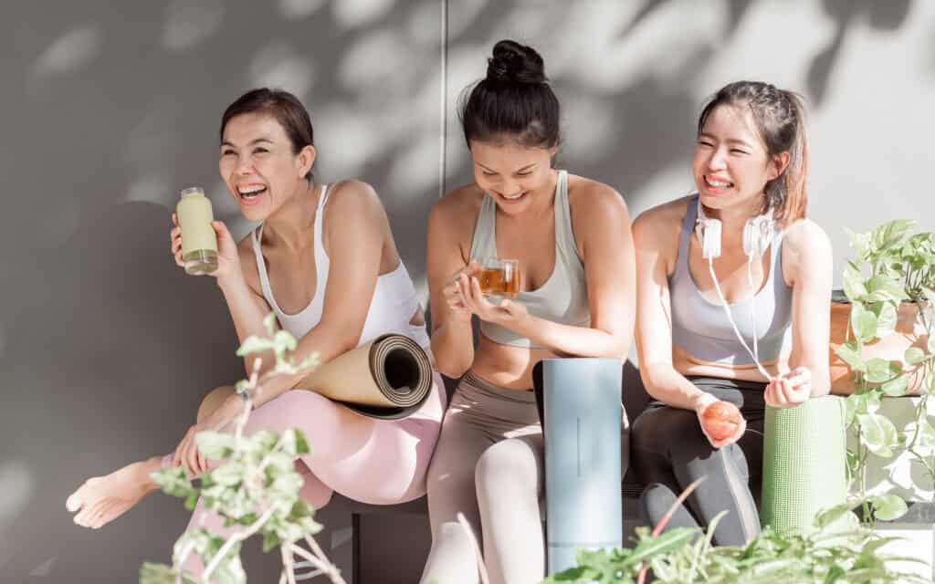 women talking and laughing together after doing exercise in yoga class at gym. Sport, Friendship and Healthy Concept.