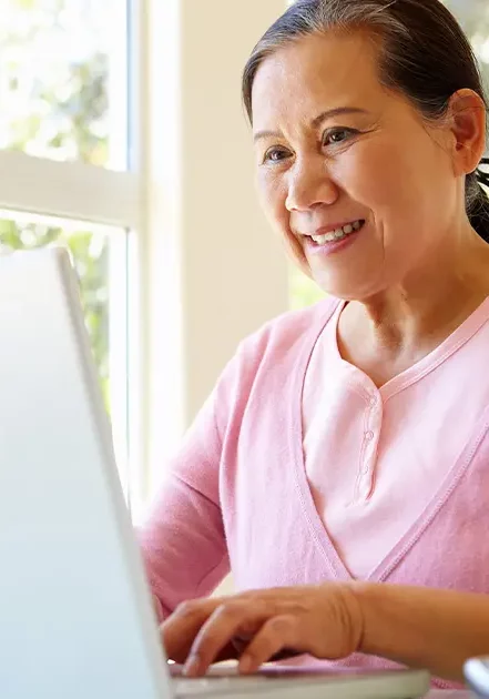 An older woman using a laptop with a smile.
